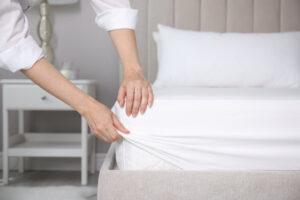 Frau, die drinnen weißes Spannbettlaken über die Matratze auf das Bett legt, Nahaufnahme