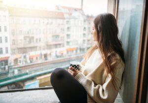 Junge Frau chillt am Fenster mit einer Tasse Kaffee